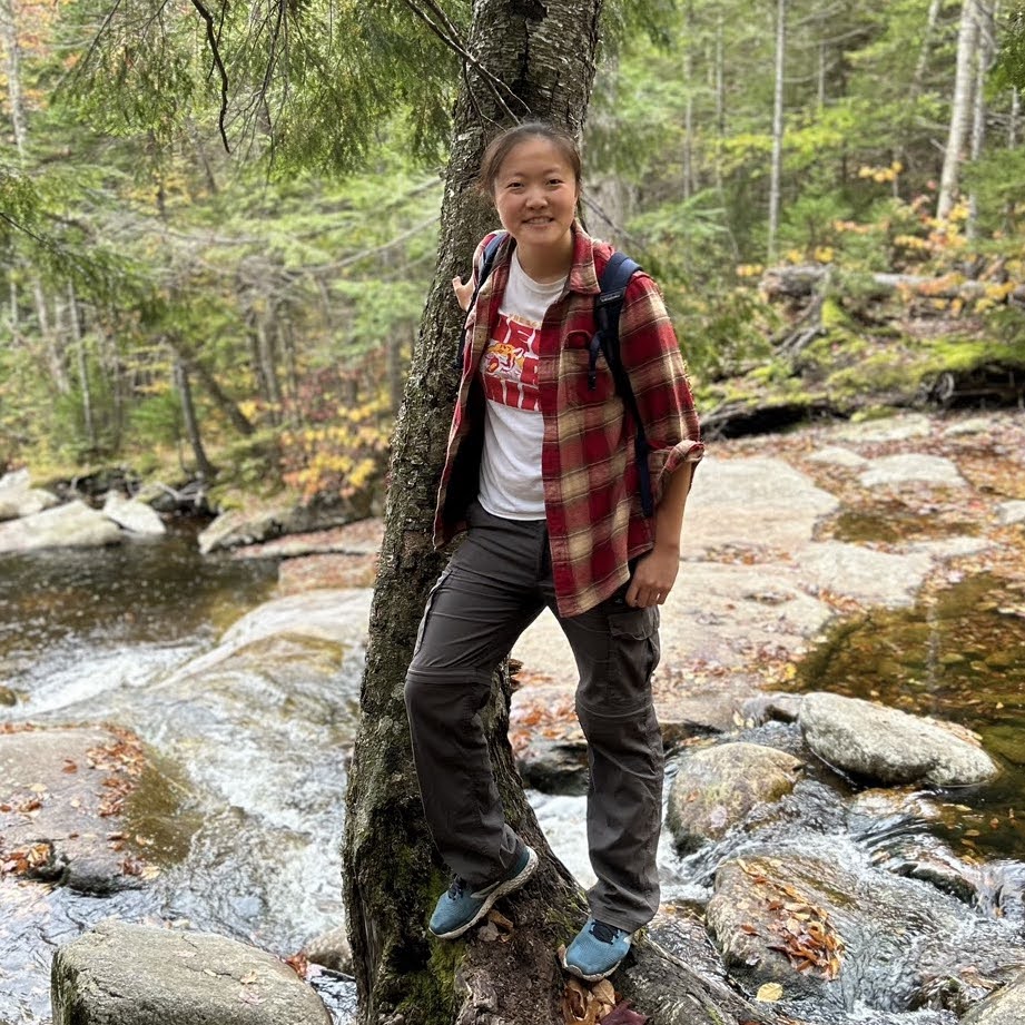 a chinese person standing by a tree in front of a stream